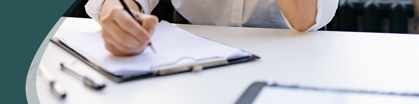 Person writing notes on clipboard and pen