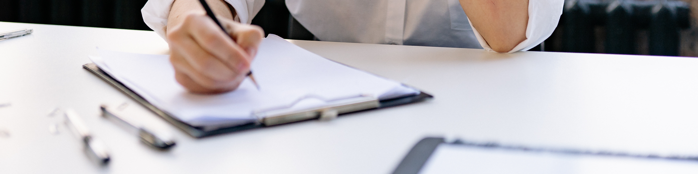 Person writing notes on a clipboard at a desk