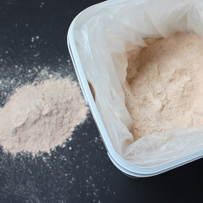 Container of flour with some spilled on a dark surface